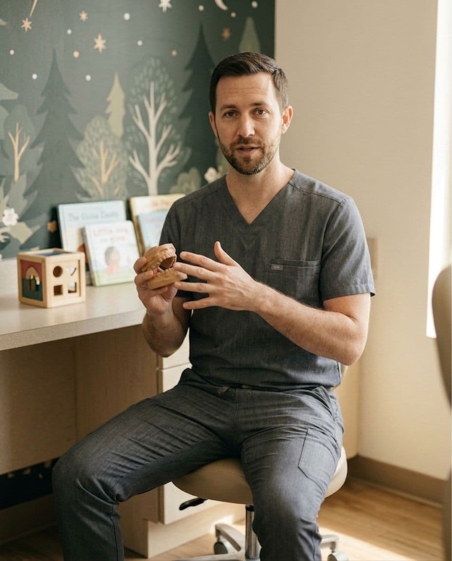 Dr. Caleb Reed in the pediatric operatory corner, holding a wooden model jaw